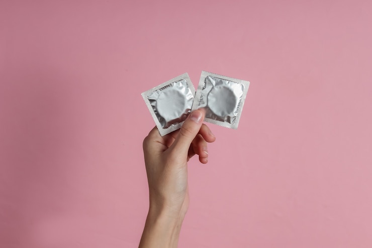 Photo female hands holding condom on pink paper