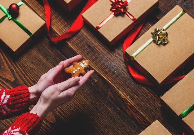 Female hands holding cookie near gift boxes over wooden table.