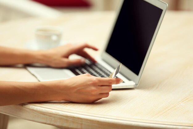 Female hands holding credit card with laptop on table close up