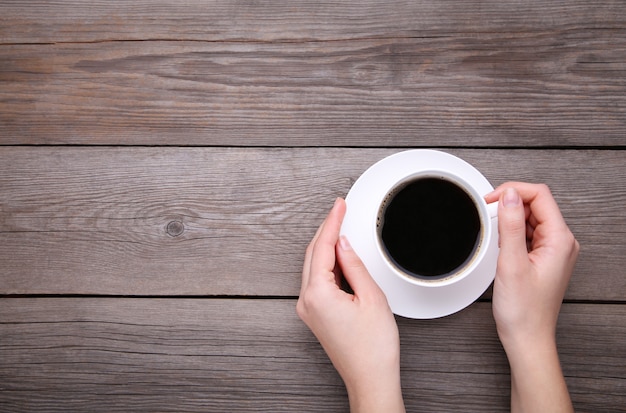 Mani femminili che tengono tazza di caffè su fondo di legno grigio.