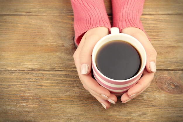 木製の背景にコーヒーのカップを保持している女性の手