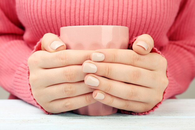 Female hands holding cup of coffee on wooden table close up