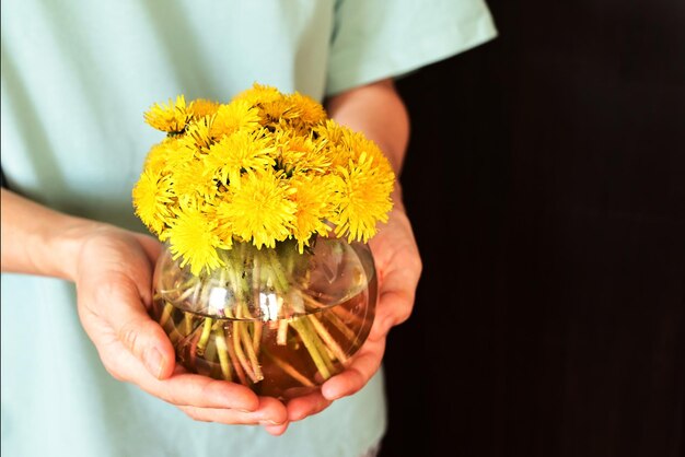 花瓶にタンポポの花を持つ女性の手 晴れた春の日に女の子が手に小さな花束を持っている