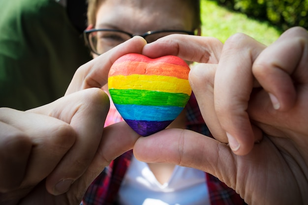 Mani femminili che tengono cuore decorativo con strisce arcobaleno.