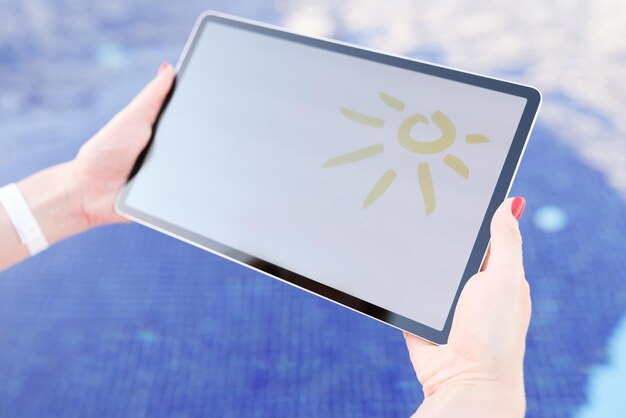 수영장 근접 촬영 위에 그려진 태양이 있는 디지털 태블릿을 들고 있는 여성 손