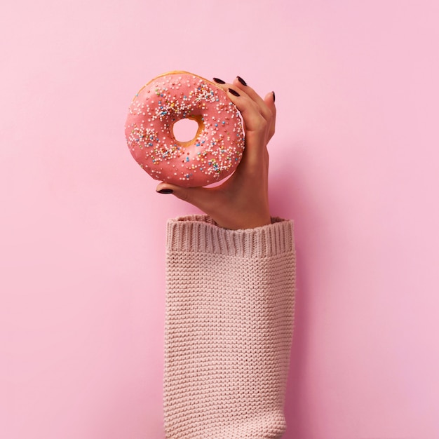 Female hands holding donut over pink background. 