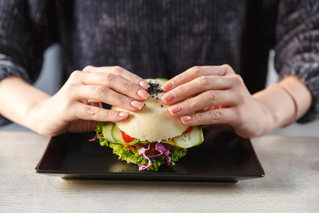 Female hands holding fresh chicken steamed bun burger with fresh cucumber salad and cabbage Fast food concept