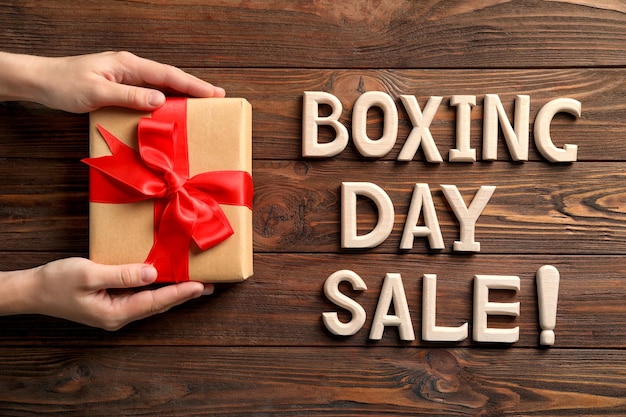 Mani femminili che tengono scatola regalo e testo boxing day sale su sfondo di legno