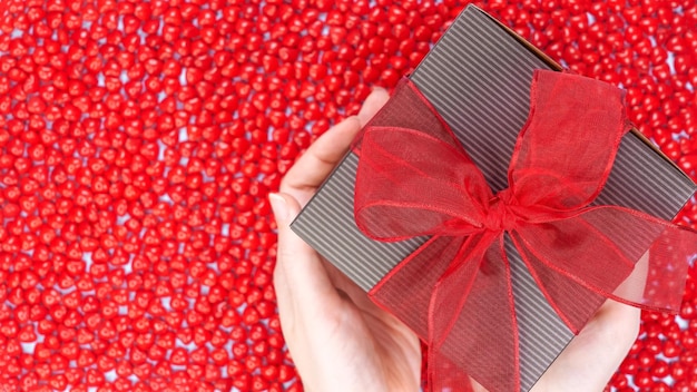 Female hands holding gift box tied with red ribbon on red candy background Valentines Day