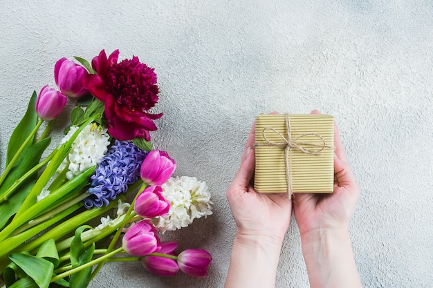 Female hands holding a gift or present box, flowers tulips, peony, hyacinth on a wooden table