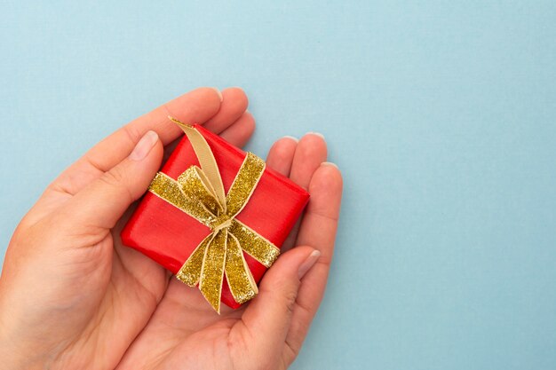 Female hands holding gift red box with golden ribbon bow