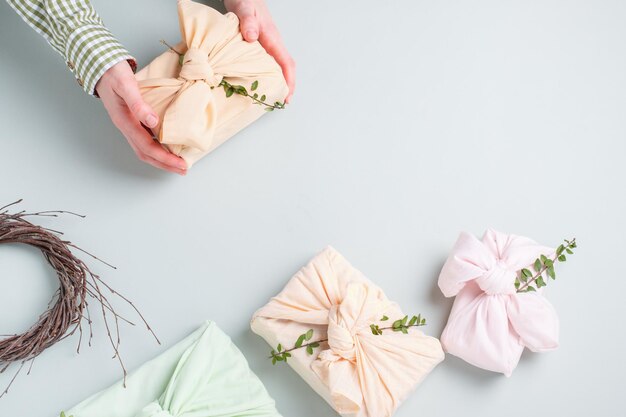 female hands holding a gift wrapped in cloth on a gray background