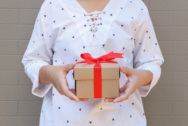 Female hands holding a gift wrapped with red ribbon