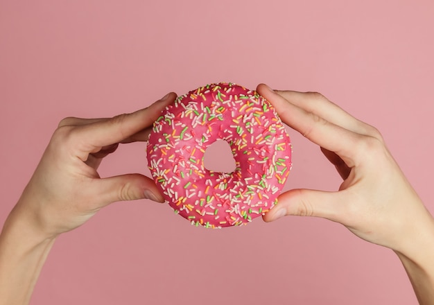 Female hands holding glazed donut on pink background. Pastel color trend.  Weight lost after holidays.Top view.