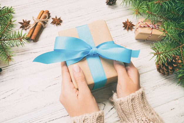 Female hands holding handmade present box in recycled paper on white wooden table 