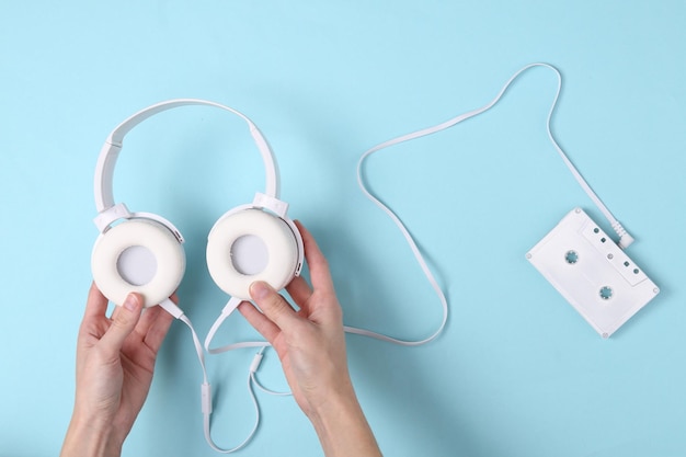 Female hands holding headphones and audio cassette on blue background Music minimal concept