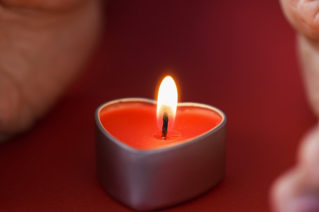 Female hands holding a heart shaped candle in dark night candlelight divination concept