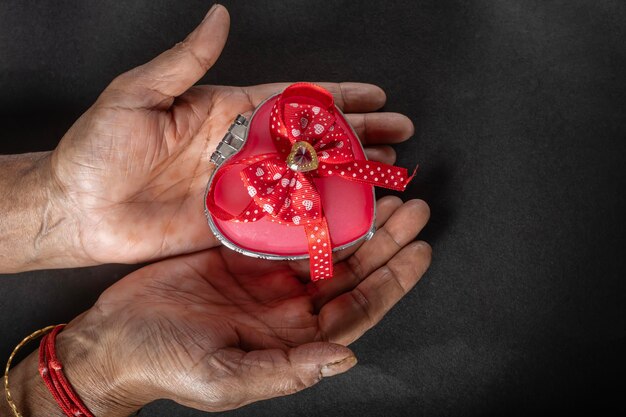Female hands holding a heart shaped gift box with a red ribbon on a black background