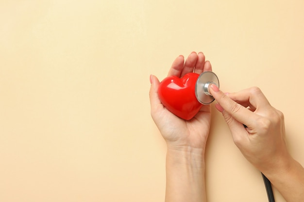 Female hands holding heart and stethoscope on beige