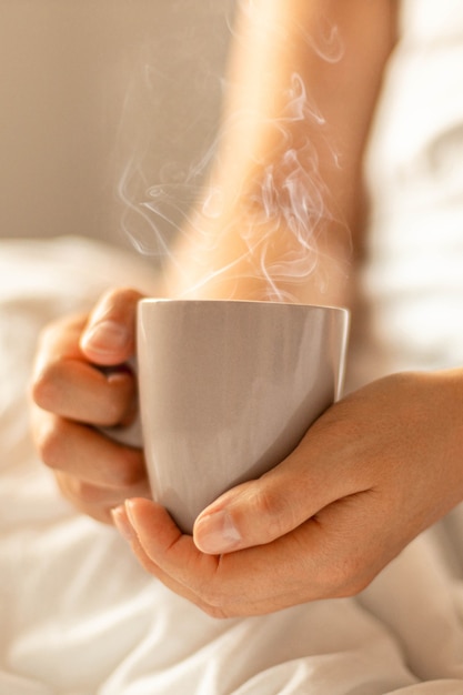 Female hands holding hot cup with aroma drink coffee or tea while sitting in bed in the early morning. Vertical video