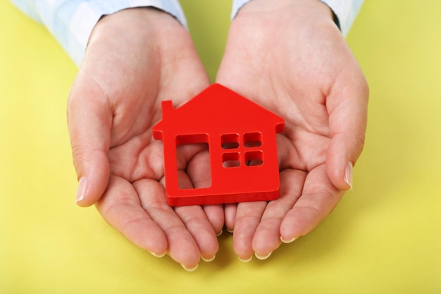 Female hands holding house on color background