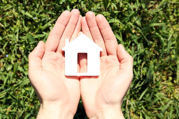 Female hands holding house over green grass background