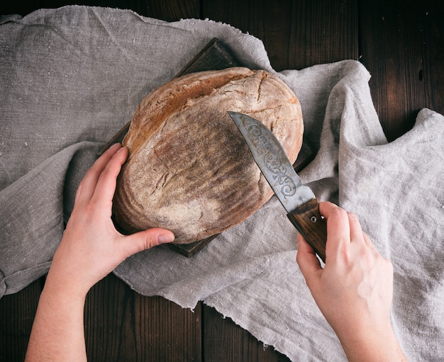 Female hands holding a knife over a baked loaf of bread