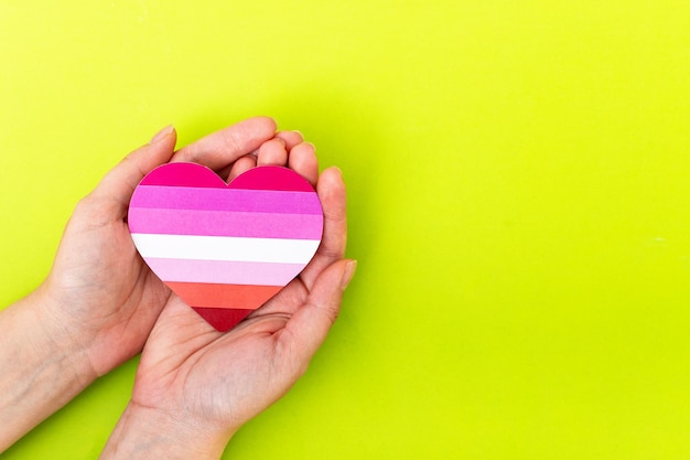 Female hands holding LGBT lesbian community flag on a heart shape Pride symbol Top view