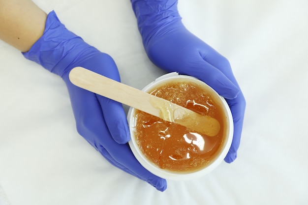 Female hands holding liquid yellow paste for shugaring on white, top view