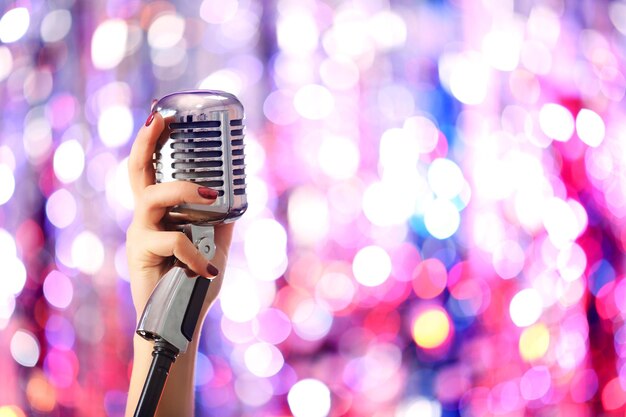 Female hands holding microphone against bright glitter background