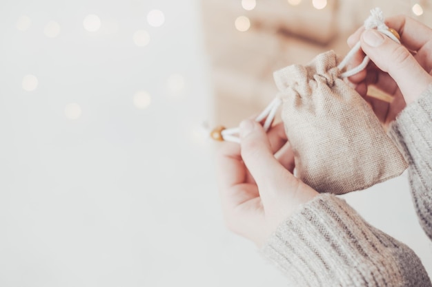 Female hands holding a mini gift bag on the background of Christmas gifts and garland