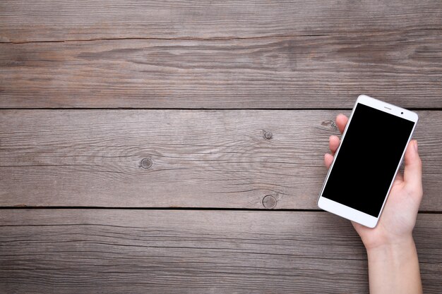 Female hands holding mobile phone with blank screen on grey wood, Smartphone on wood table.