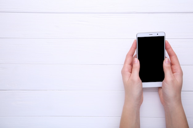 Female hands holding mobile phone with blank screen on white wood, Smartphone on wood table.