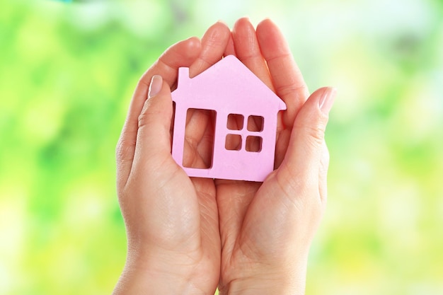 Female hands holding model of house on bright background