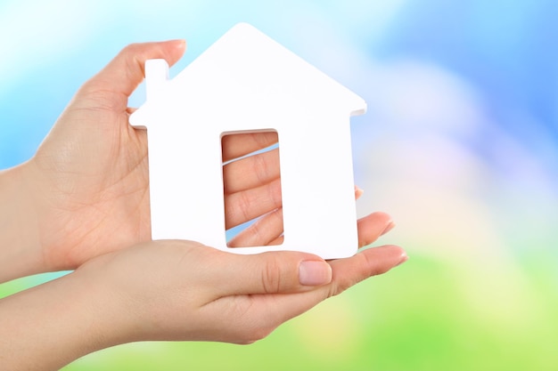 Female hands holding model of house on bright background