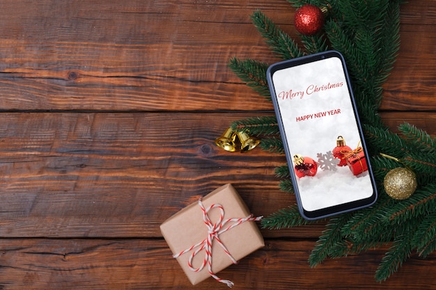 Female hands holding modern smartphone with mockup on wooden vintage table with christmas