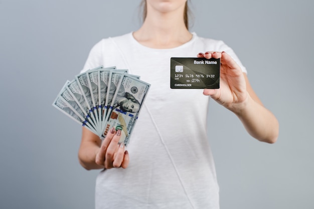 Female hands holding one hundred dollar bills and credit card isolated over grey