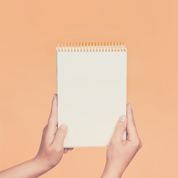 Female hands holding open a blank Notepad for notes on the peach wall. Toned.