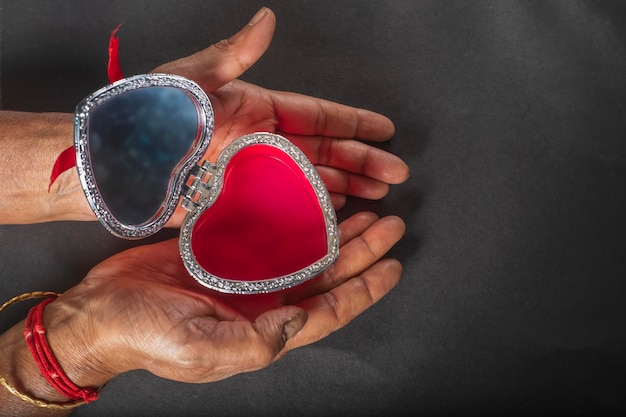 Female hands holding open heart shaped jewelry box on black background Valentines Day