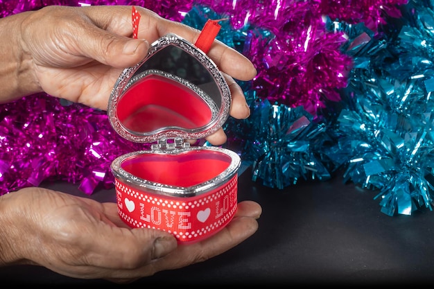 Female hands holding open heart shaped jewelry box on tinsel background