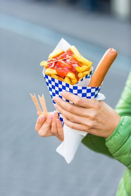 ホットソーセージとフライドポテトと紙のコーンを保持している女性の手