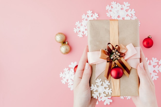 Female hands holding present with bow on pink background.