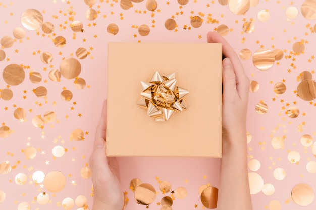 Female hands holding present with golden bow. Top view