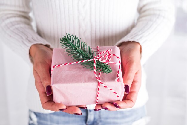 Female hands holding present with red bow on white . Festive backdrop for holidays