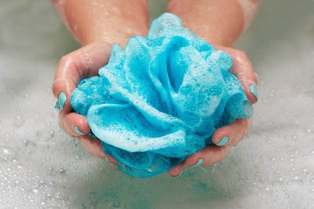 Mani femminili che tengono un panno sintetico morbido rotondo in bagno con acqua. primo piano delle mani. trattamento termale, cura del corpo, fondo dell'acqua.