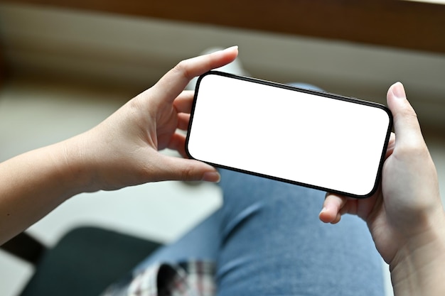 A female hands holding a smartphone white screen mockup in a\
horizontal position