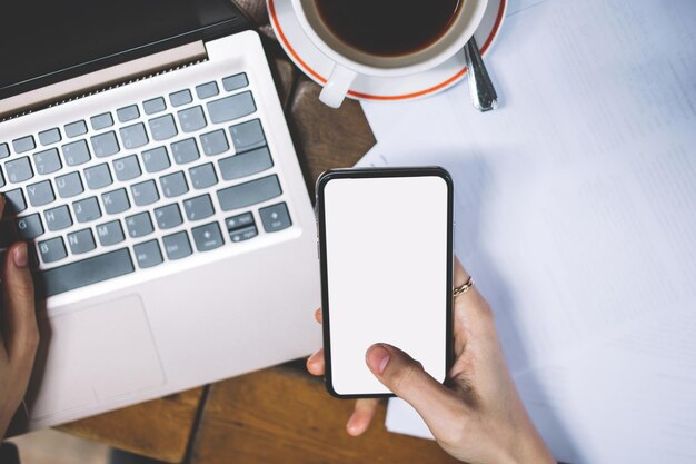 female hands holding smartphone with big screen front laptop keyboard working with documents