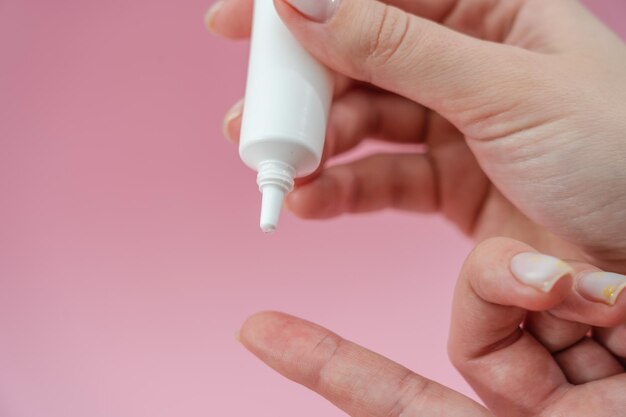 Female hands holding and squeezing tube of cream gel on pink\
background sosmetic bottles for beauty or medicine products