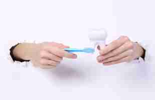 Photo female hands holding tooth model and toothbrsh through torn hole white paper oral cavity care concept art minimalism