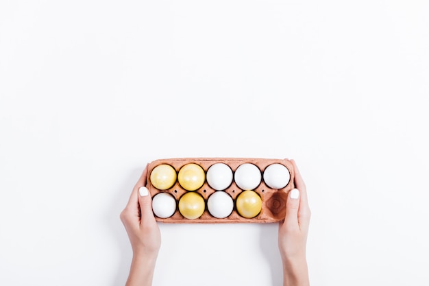 Female hands holding a tray with yellow Easter eggs on white background